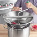 A person using a Garde stainless steel rotary food mill to press raspberries into a metal bowl.