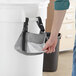 A person using a Lavex Gray trash bag dispenser to hold a bag from a trash can.