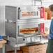 A woman putting pizza in a large Avantco countertop oven.