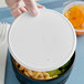 A hand holding a Cambro speckled white plastic lid over a bowl of macaroni and cheese.