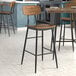 A Lancaster Table & Seating black barstool with a vintage wood seat and metal frame.