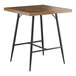 A Lancaster Table & Seating Mid-Century bar height table with black metal legs and a wooden top.
