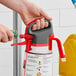 A hand holding a red and black plastic SC Johnson Professional TruFill dispenser head sprayer.