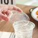 A hand placing a World Centric PLA plastic lid on a clear plastic cup.