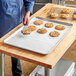 A person putting chocolate chip cookies on a tray lined with a 16" x 24" Full Size silicone coated parchment paper sheet.