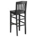 A black Lancaster Table & Seating wood school house bar stool with a backrest.