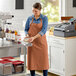 A woman in an Acopa Ashville Cinnamon Linen Adjustable Bib Apron with 3 Pockets standing in a kitchen.