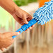 A person using a Lavex Flex Wand Duster with a blue microfiber sleeve on the end.