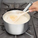 A person using a Vollrath Arkadia sauce pan and wooden spoon to stir liquid.