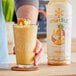 A hand holding a glass of Smartfruit Aloha Pineapple Puree Beverage with pineapples on top.