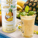A white bottle of Smartfruit Aloha Pineapple Puree next to a glass of yellow smoothie.