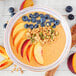 A bowl of Smartfruit Tropical Harmony smoothie with peaches and blueberries on a table.