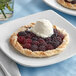A white Toque Tarte Flambee crust with blackberries and ice cream on a plate.