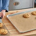 A person using a large knife to cut cookies on a parchment paper-lined tray.