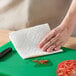 A hand using a Bounty paper towel to wipe off sliced tomatoes on a cutting board.