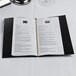 A black Menu Solutions wine list cover on a table with white text inside.