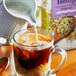 A glass mug of coffee with a pitcher pouring Pacific Foods Unsweetened Hemp Milk into it.