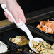 A hand holding a white Cambro salad bar spoon over a bowl of food.
