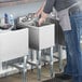 A person standing next to a Steelton underbar hand sink on a counter in a professional kitchen.