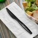 A Stalk Market black CPLA knife on a napkin next to a bowl of salad.