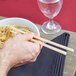 A person holding Town ivory plastic chopsticks in a bowl of noodles.