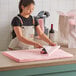 A woman in a black apron cutting a light pink Lavex tissue paper sheet on a table.