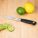 A Mercer Culinary Genesis forged utility knife with a black handle next to a lime and lemon.