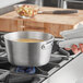 A person holding a Vollrath Wear-Ever aluminum sauce pan with liquid in it over a stove.
