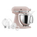 A KitchenAid Artisan series countertop mixer in pink with a white bowl and whisk.