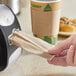 A hand pulling a Tork Xpressnap Fit Universal dispenser napkin from a holder on a counter.