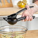 A person using a black handheld lemon squeezer over a bowl of salad.