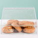 A clear plastic Cal-Mil food bin with bagels in it on a counter in a bakery display.