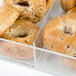 A clear Cal-Mil food bin with bagels and a removable divider.