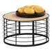 A black metal and bamboo display riser holding a plate of cookies on a round wooden table.