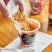 A hand pouring granola into a container of Del Monte strawberry yogurt.