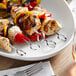 A skewer of grilled meat and vegetables on a Vollrath stainless steel skewer on a table.