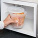 A hand holding a Pactiv translucent round squat deli container with food in a microwave.