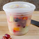 A Pactiv translucent plastic deli container filled with fruit, with a yellow and red lid.