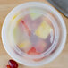 A translucent Pactiv plastic deli container filled with fruit on a counter.