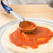 A person using a Vollrath blue round portion spoon to spread sauce on a pizza.