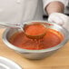 A person using a Vollrath Jacob's Pride blue solid round Spoodle to serve red sauce.