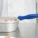 A person using a Vollrath blue handled portion spoon to serve food.