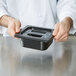 A hand using a Cambro black plastic container lid to cover food.