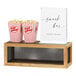 A Cal-Mil black metal and oak wood display riser with boxes of popcorn on the wood shelf.