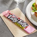 A pink Laffy Taffy candy next to a sandwich on a napkin.