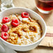 A bowl of oatmeal with raspberries and almonds and a brown sugar packet on a table.