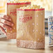 A close-up of two hands holding brown Carnival King popcorn bags with red and white designs.
