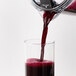 A glass of red juice being poured into a Breville juice extractor.