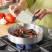A person cooking mussels in a Vollrath Wear-Ever saute pan on a stove.