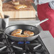 A person cooking chicken in a Vollrath stainless steel non-stick fry pan on a stove.